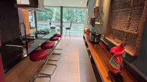 A modern kitchen with a bar area, red bar stools, a large window, and a decorative woven wall. - 5-Bedroom 6000SF wood and glass retreat in Atlanta, surrounded by greenery.   (Atlanta)