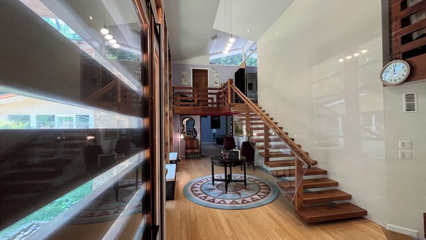 A spacious interior with a wooden staircase, a round rug, and a view through a glass door. - 5-Bedroom 6000SF wood and glass retreat in Atlanta, surrounded by greenery.   (Atlanta)