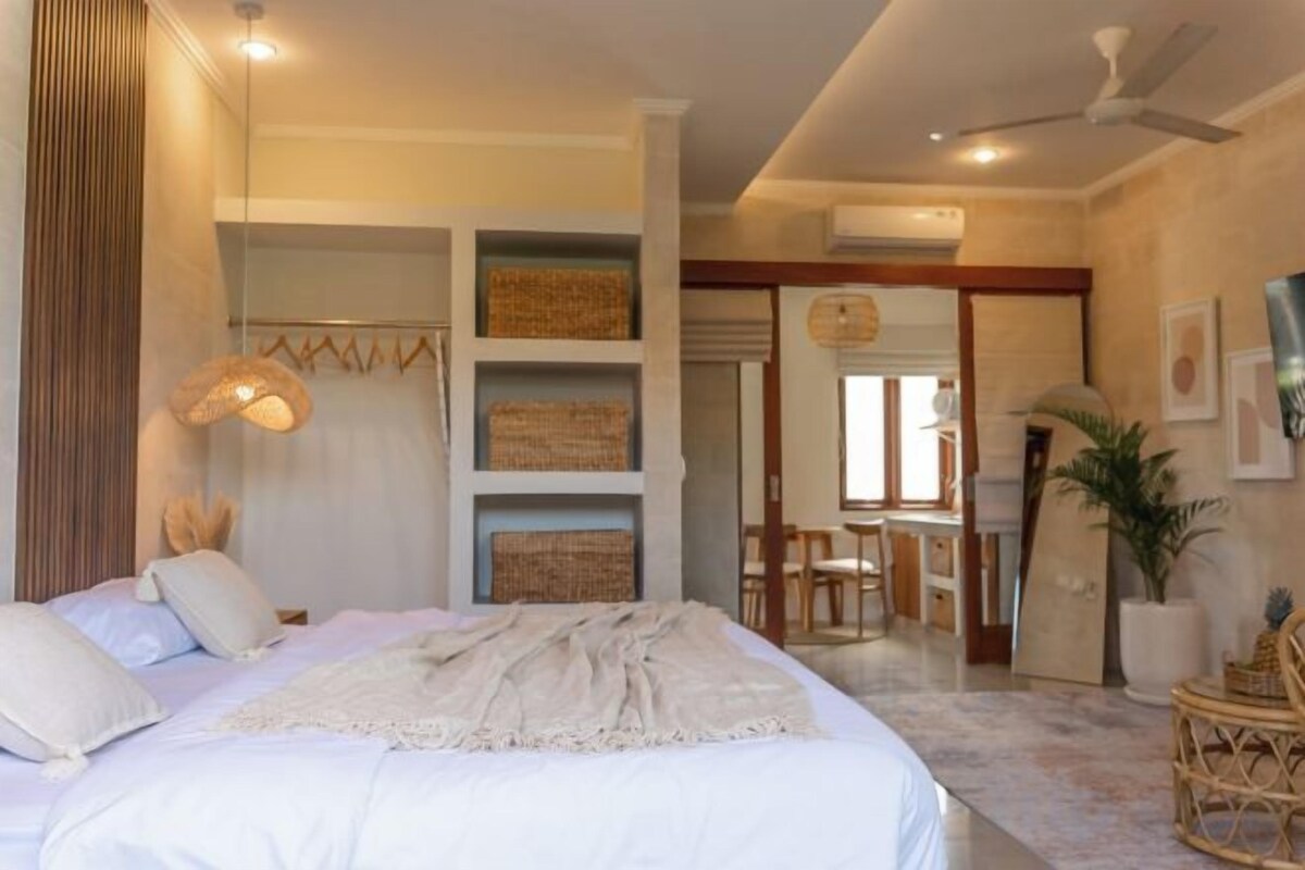A bedroom with a large bed, a ceiling fan, and a view of a dining area.