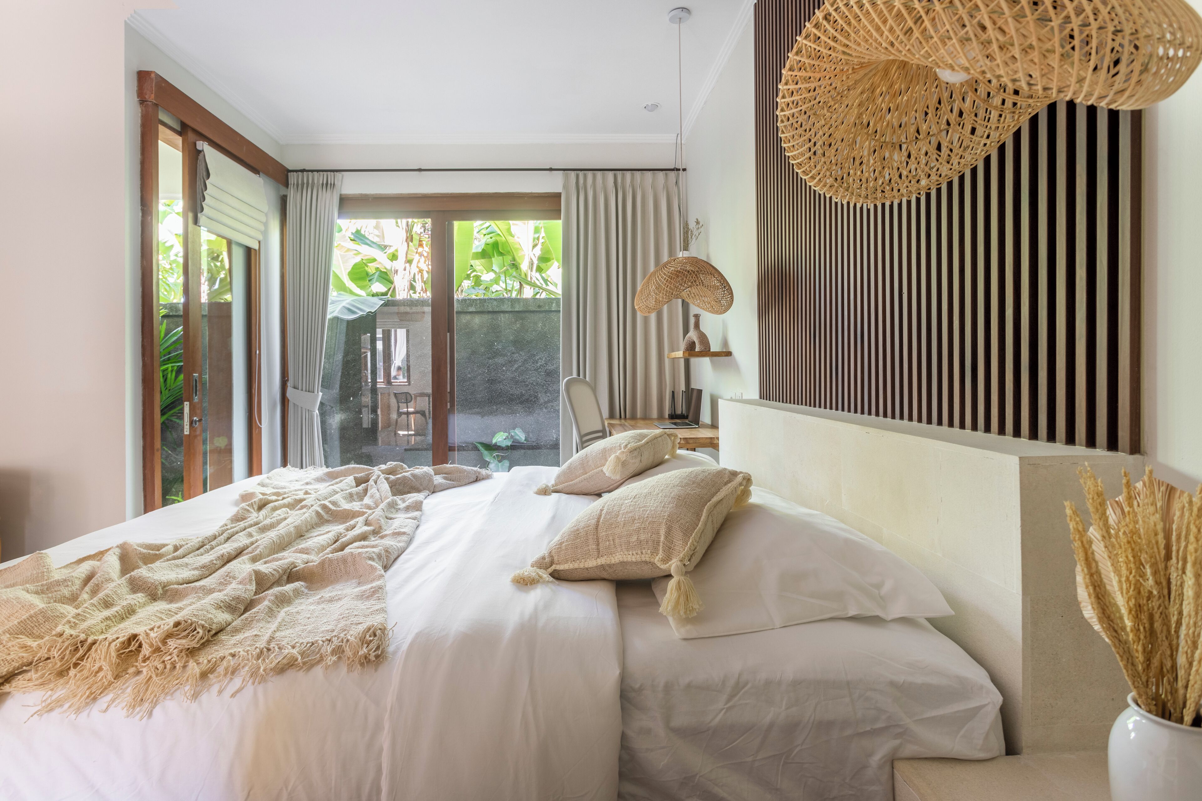 Quarto com cama grande, vista para o verde lá fora e luminária de vime.