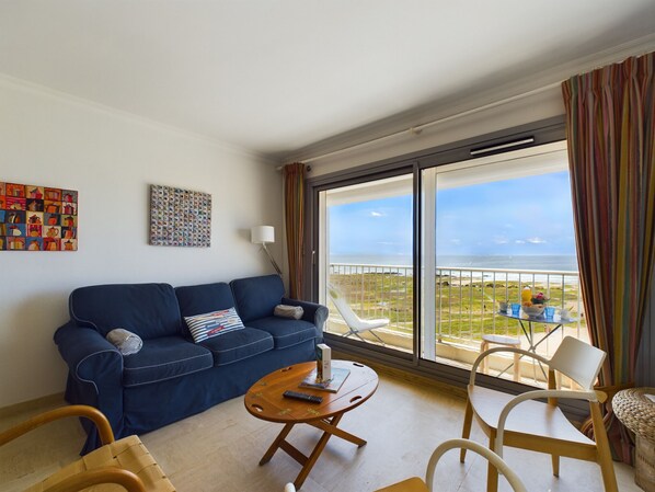 A living room with a blue sofa, a wooden coffee table, and a view of the sea through large windows.