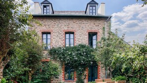 Un edificio de piedra con fachada de ladrillo, varias ventanas y un jardín con un banco.