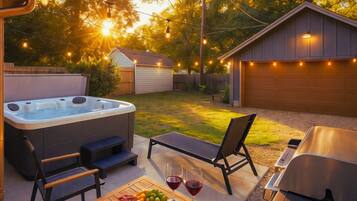 Un patio exterior con un jacuzzi, una parrilla y una mesa con comida y bebidas.
