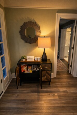 Un couloir avec une console en bois sur laquelle sont posés un panneau d’accueil, une lampe et une petite plante.