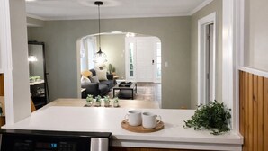 A modern kitchen with a central island, a dining area with a sofa and coffee table, and a view into the living room. - Hot Tub+Arcade / Fire Pit Retreat Near Monon Trail (Indianapolis)