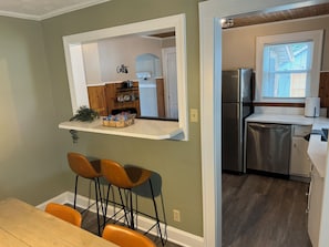 Eine Küche mit Einbaukühlschrank, Spüle und einem Fenster mit Jalousien. Es gibt eine Bar mit Hockern und ein Regal mit Snacks.