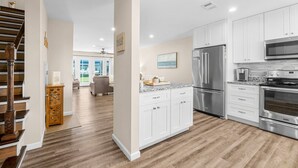 A modern kitchen with white cabinets, stainless steel appliances, and a wooden staircase.