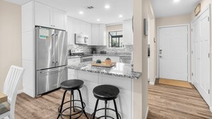 A modern kitchen with white cabinets, stainless steel appliances, a granite countertop, and two bar stools.