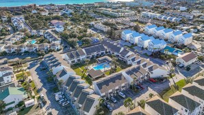 An aerial view of a coastal residential area with multiple buildings, a swimming pool, and a clear view of the ocean.