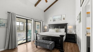 A bedroom with a large bed, a bench, a nightstand, and a view of the outdoors through a sliding door.