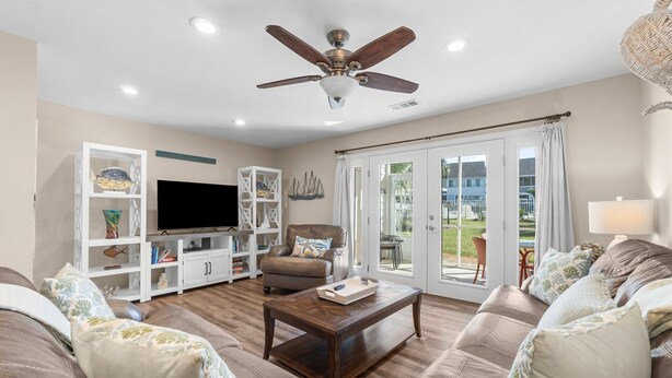 A living room with a brown leather sofa, a wooden coffee table, a ceiling fan, and a TV on a white cabinet.