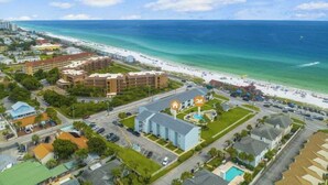 An aerial view of a coastal area with a beachfront hotel, a parking lot, and a road leading to the beach. - 🏖️Tradewinds 21 - Coastal Charm | Easy Beach Access | Steps to Pool🏖️ (Miramar Beach)