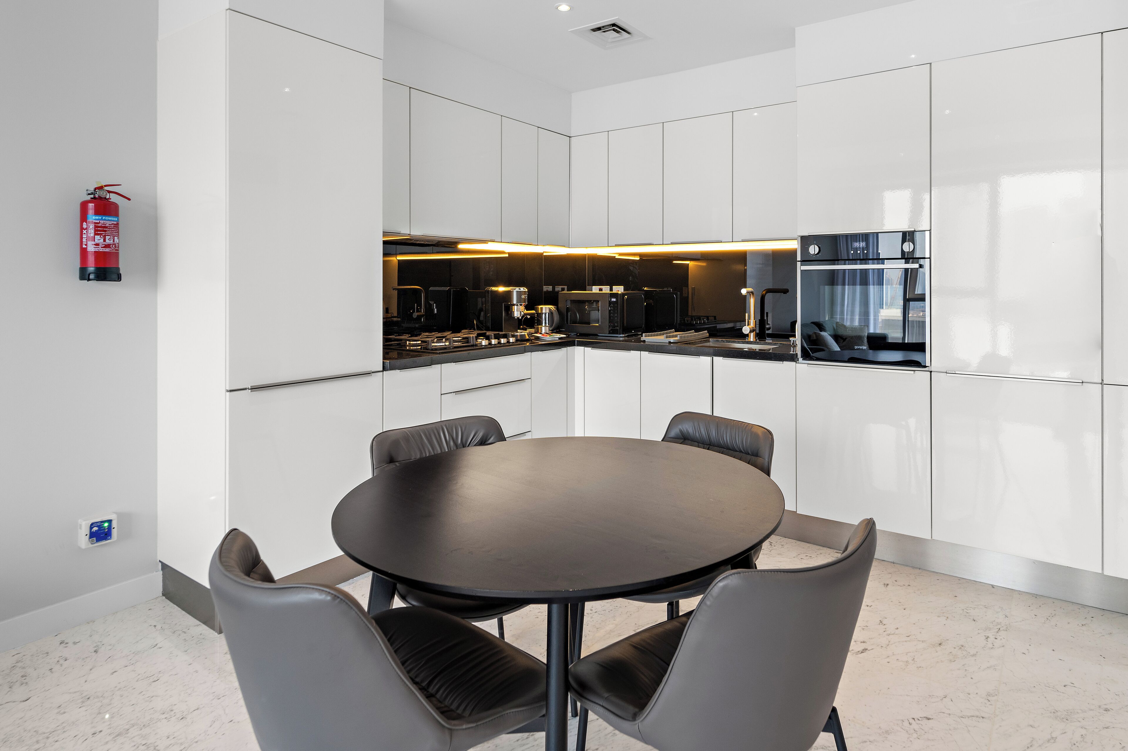 A modern kitchen with white cabinets, a black countertop, and a round dining table with chairs.