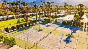 Ein Tennisplatz, umgeben von Palmen und einem Pool, mit Bergen im Hintergrund.