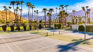 Ein Tennisplatz mit mehreren Spielfeldern, umgeben von Palmen und einer Bergkulisse.