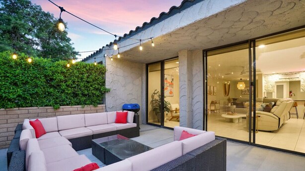 An outdoor living area with a sectional sofa, a glass door leading to a modern interior, and string lights. - The Springs: Luxury Resort Living, Palm Springs (Palm Springs)