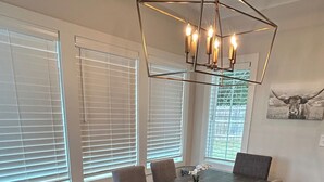 Un coin repas avec une table en bois foncé, six chaises rembourrées et un lustre aux motifs géométriques.