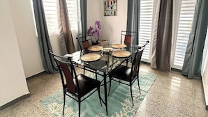 Zona pranzo con tavolo in vetro, sedie nere, sottopiattino intrecciato e ventola a soffitto.