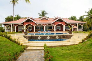 Ein großes Haus mit Swimmingpool, überdachter Terrasse und üppiger Bepflanzung.