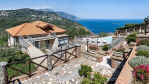 Une propriété située sur une colline, dotée d’un escalier en pierre, d’une piscine et offrant une vue sur la mer.