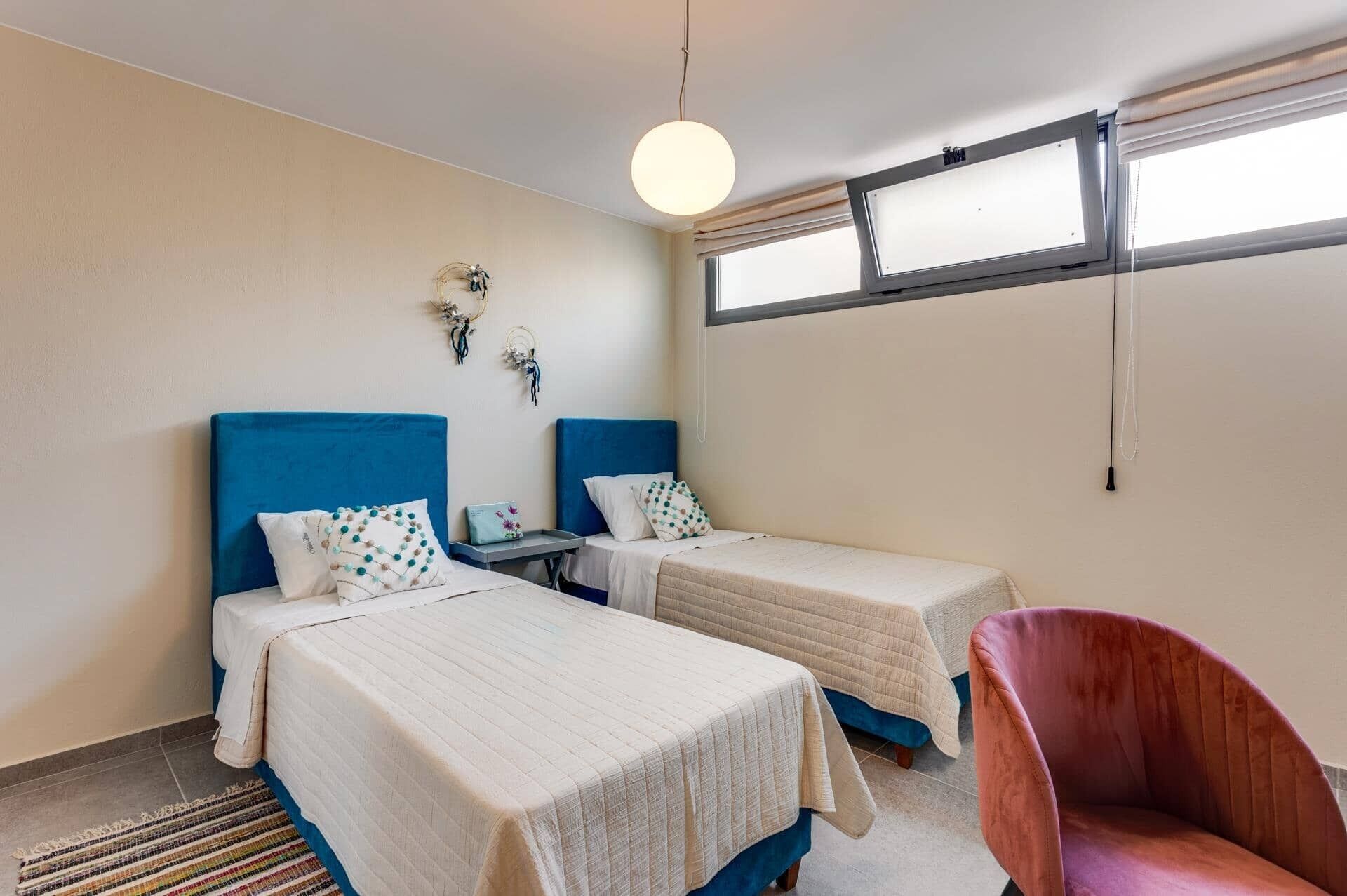 Una habitación con dos camas, una silla, un ventanal y una lámpara colgante.