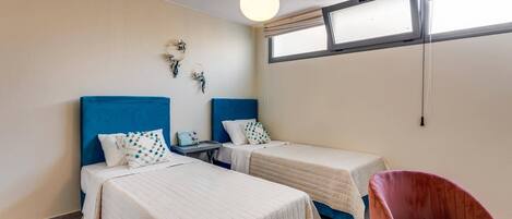 Una habitación con dos camas, una silla, un ventanal y una lámpara colgante.