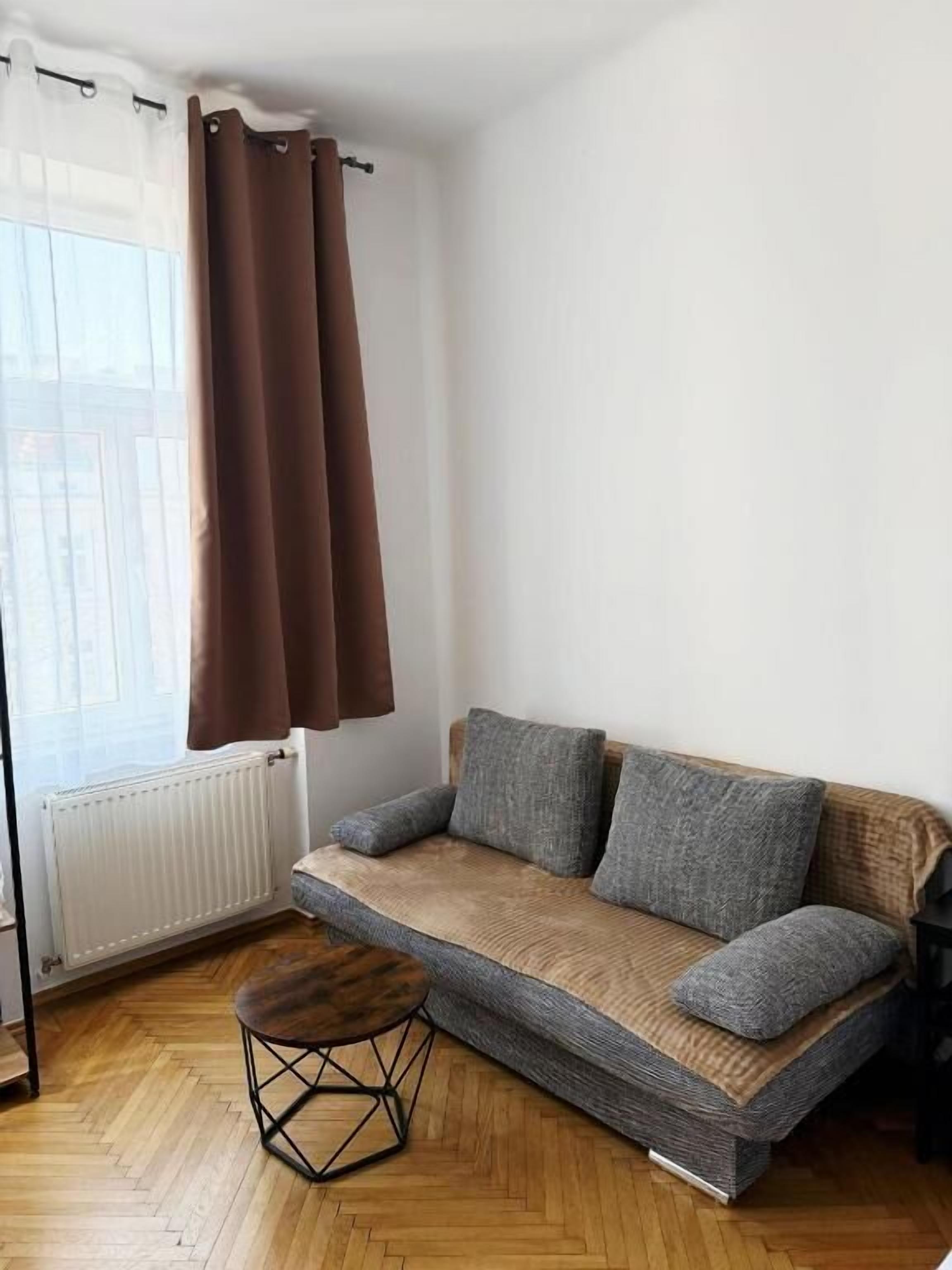 Une pièce comprenant un canapé, un petit tabouret en bois, un radiateur et une fenêtre avec des rideaux.