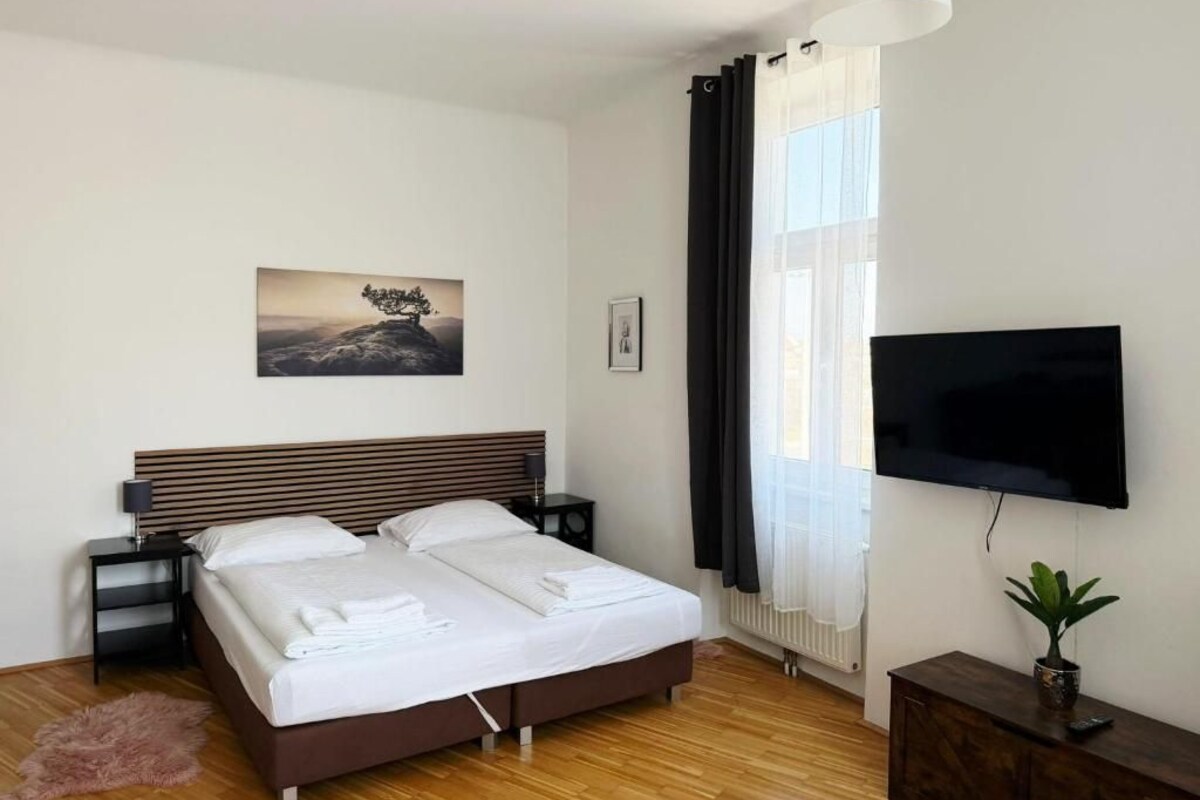 A bedroom with a bed, a TV, a plant, and a painting on the wall.