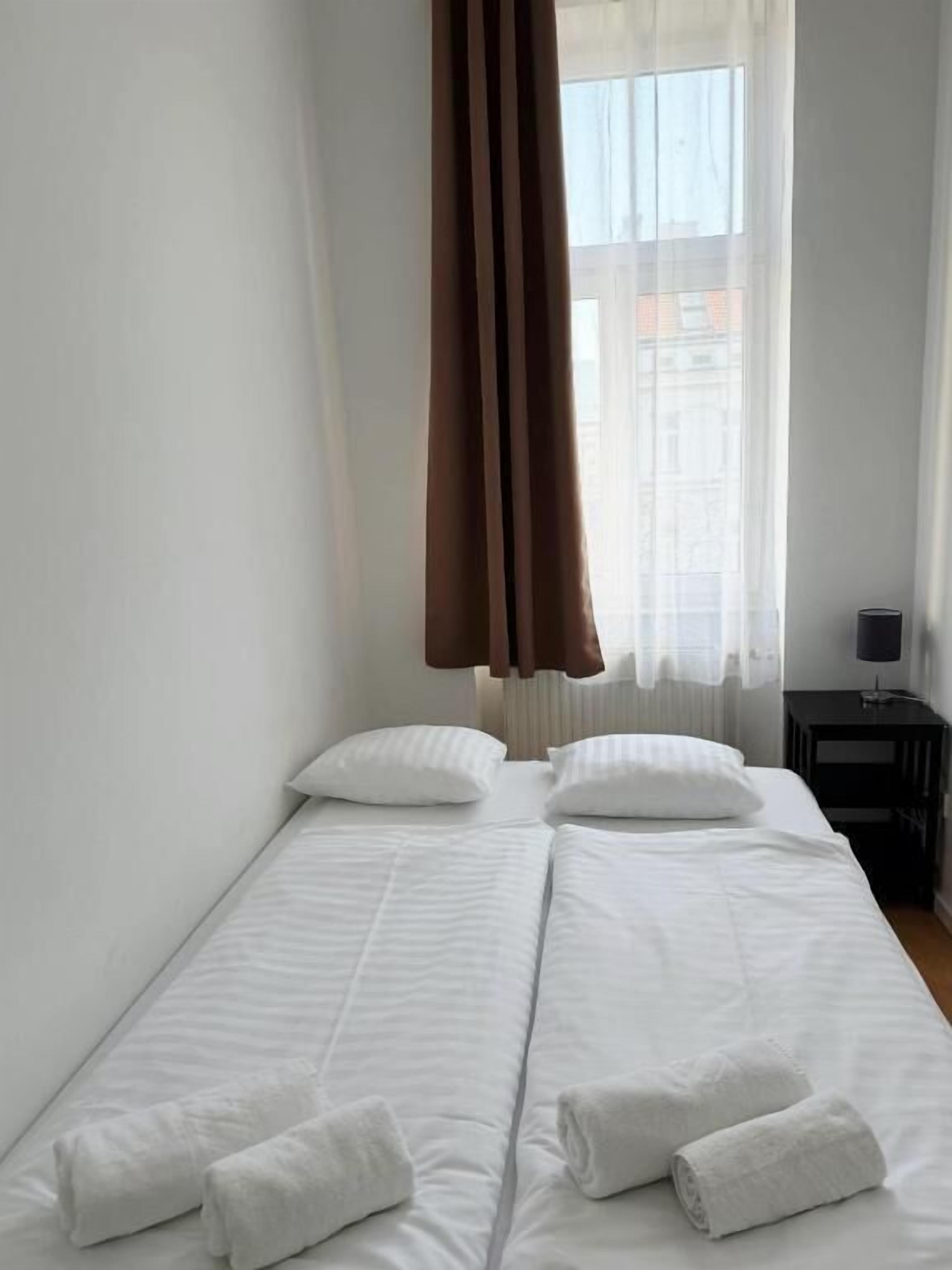 Una camera d'albergo con un letto, cuscini, un comodino e una finestra con tende.