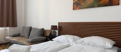 A hotel room with a bed, a chair, a nightstand, and a painting on the wall.
