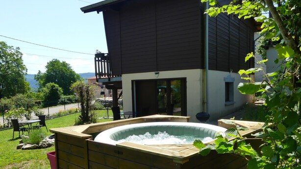 Un bain à remous installé dans une structure en bois, avec vue sur une maison et un jardin.