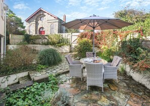 Relax under the shade of a large umbrella, surrounded by lush climbing plants and a historic building in the background.