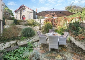 Relax under the shade of a large umbrella, surrounded by lush climbing plants and a historic building in the background.
