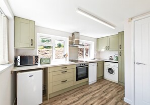 Compact kitchen with modern design, light wood flooring, and neutral cabinetry, featuring a microwave, oven, dishwasher, and washing machine.