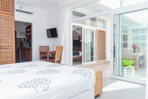 Et moderne hotelværelse med en stor seng, et fjernsyn, en skydedør til en balkon og et tekøkken.