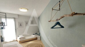 Une chambre avec deux lits, un fauteuil suspendu et une étagère fixée au mur.