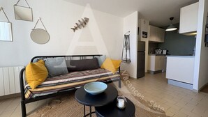 Un salon moderne avec un canapé noir, une table basse ronde et un coin cuisine à l’arrière-plan.