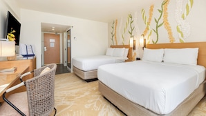Une chambre d’hôtel avec deux lits, un bureau avec une lampe, un fauteuil en osier et un mur décoré d’œuvres d’art florales.