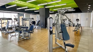 Une salle de sport équipée de divers appareils d’exercice, dotée d’un éclairage au plafond de couleur vert vif et d’un plancher en bois.