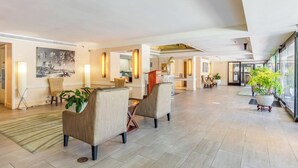 Un hall d’entrée spacieux avec un plafond haut, une grande peinture au mur et un coin salon avec des fauteuils et une table basse.