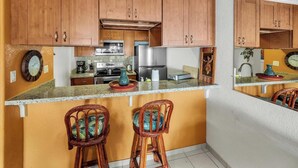 A compact kitchen with wooden cabinets, a granite countertop, and two wicker bar stools.