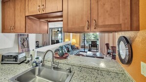 A kitchen with wooden cabinets, a granite countertop, a stainless steel sink, a toaster, and a dining area with a table and chairs.