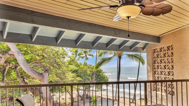 A covered outdoor seating area with a view of the ocean and palm trees.