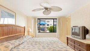 Une chambre d’hôtel équipée d’un lit, d’une télévision, d’un ventilateur de plafond, d’une fenêtre avec des rideaux et offrant une vue sur l’extérieur.