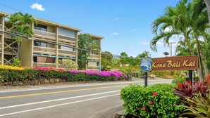 A multi-story hotel with balconies, a sign reading "Kona Bali Kai," and a road in front.