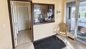 A reception area with a closed door, a notice board, a chair, and a black mat.