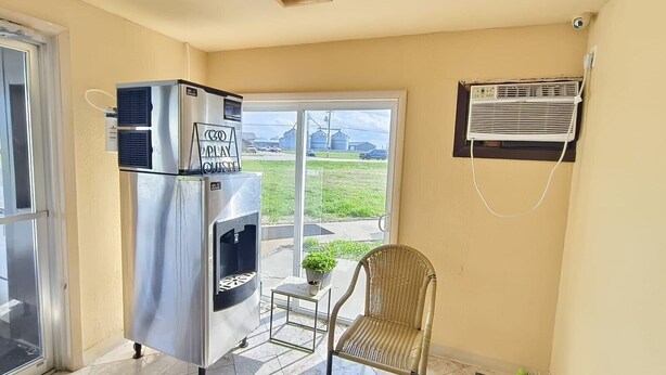 A balcony with a stainless steel refrigerator, a wicker chair, and an air conditioning unit.