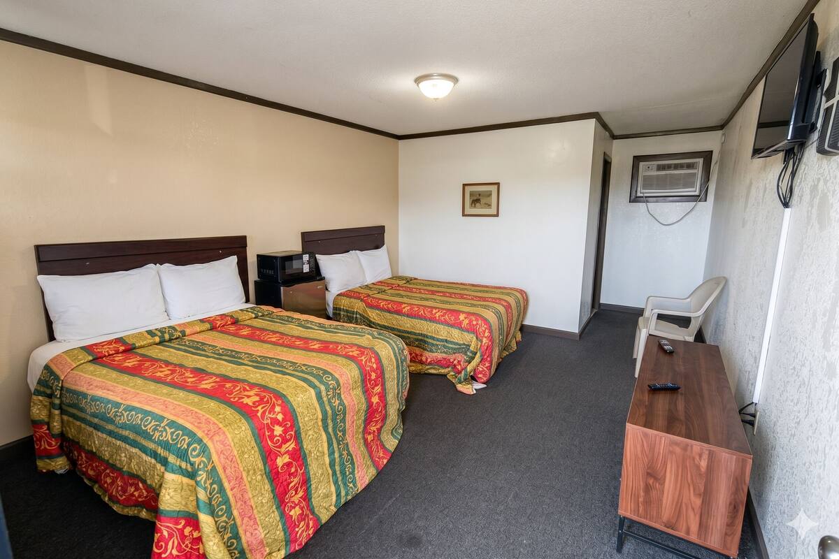 Une chambre d’hôtel avec deux lits, un bureau, une chaise, un appareil de climatisation et un téléviseur.