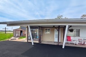 Ein eingeschossiges Gebäude mit überdachter Veranda, einer kleinen angeschlossenen Garage und einer Terrasse mit Gartenmöbeln.