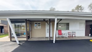 A building with a covered entrance, a small patio with chairs, and a window with blinds.